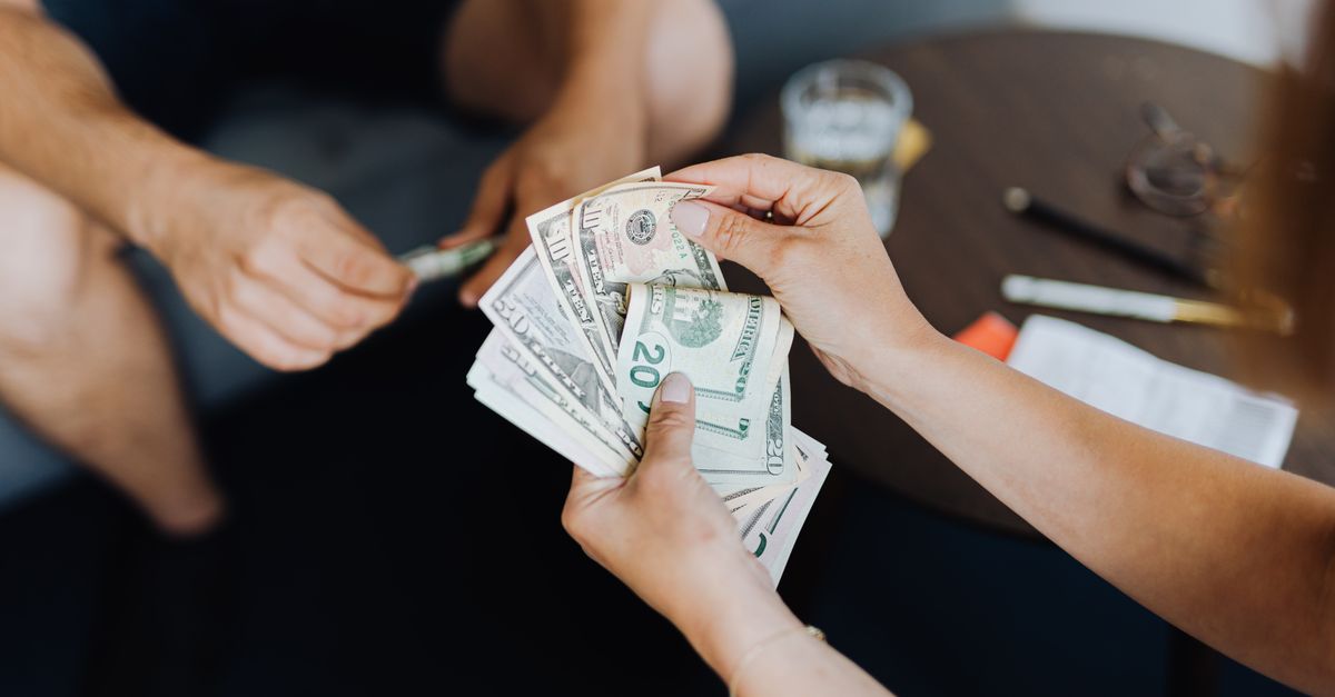 Close-up of people handling and counting US dollar bills indoors.